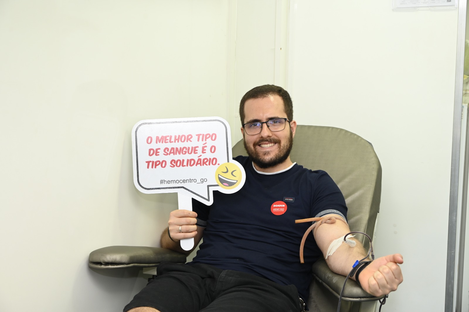 Imagem ilustrativa de um homem realizando uma doação de sangue e segurando uma placa com a escrita "O melhor tipo de sangue é o tipo solidário."