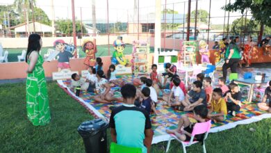 Imagem ilustrativa do programa Cine Leitura do Bem. Na imagem, crianças escutam histórias de literatura infantil em uma praça pública.