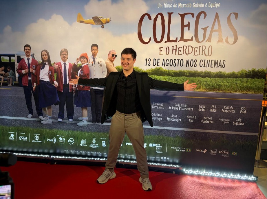 Imagem ilustrativa de João Vitor de Paiva em frente ao pôster do filme Colegas e o Herdeiro.