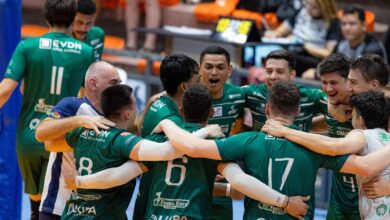 Imagem ilustrativa de jogadores de vôlei se reunindo em círculo em um jogo dos jogos universitários.
