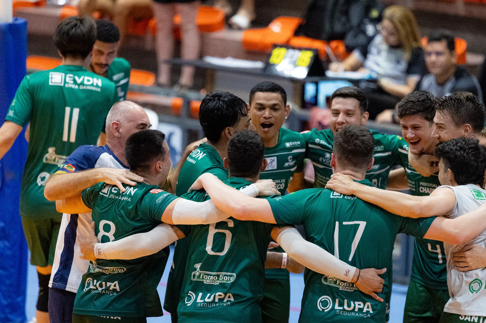 Imagem ilustrativa de jogadores de vôlei se reunindo em círculo em um jogo dos jogos universitários.